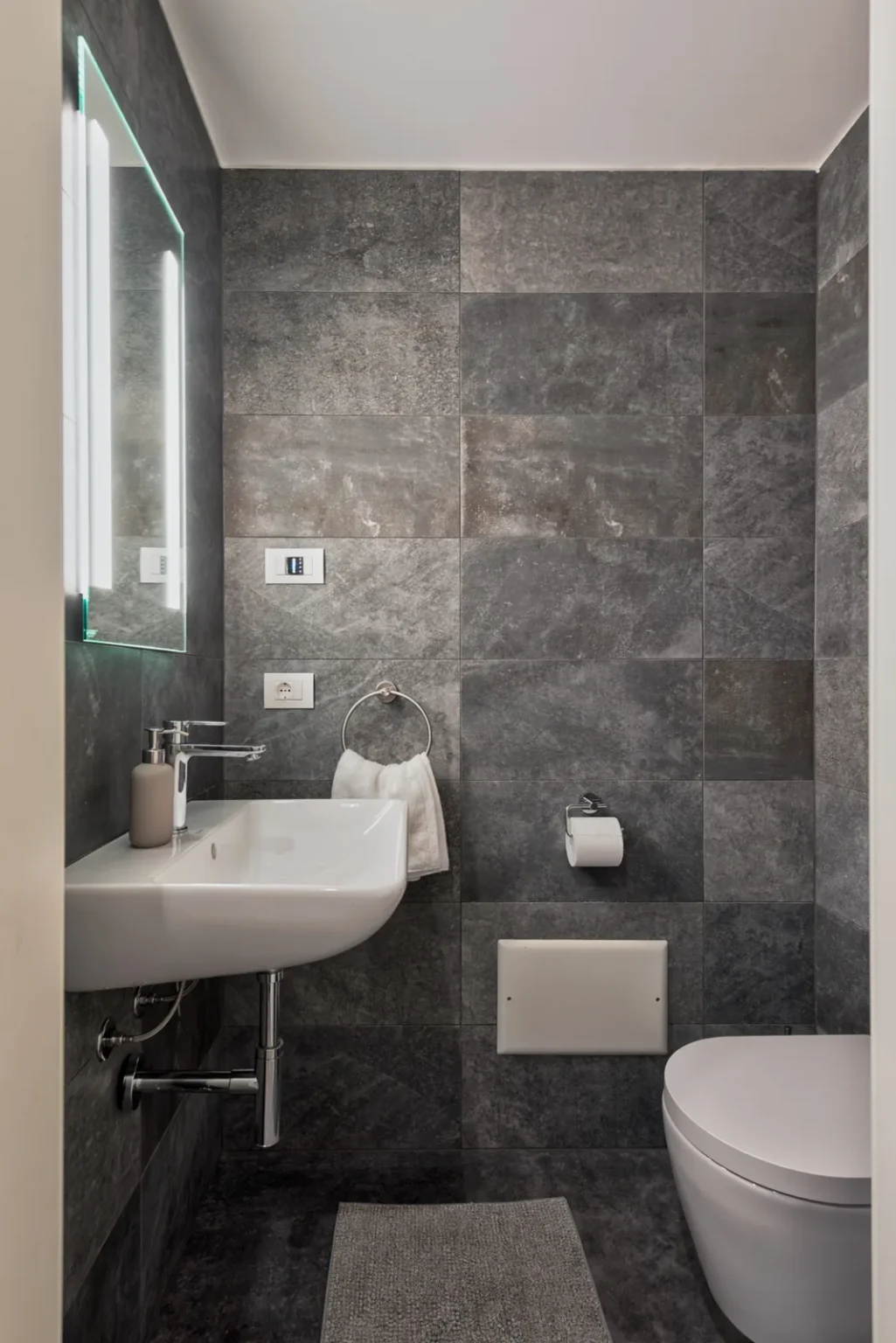 Small washroom with a wall-mounted basin, an illuminated mirror and a wall-hung toilet. | Only on SopranoVillas